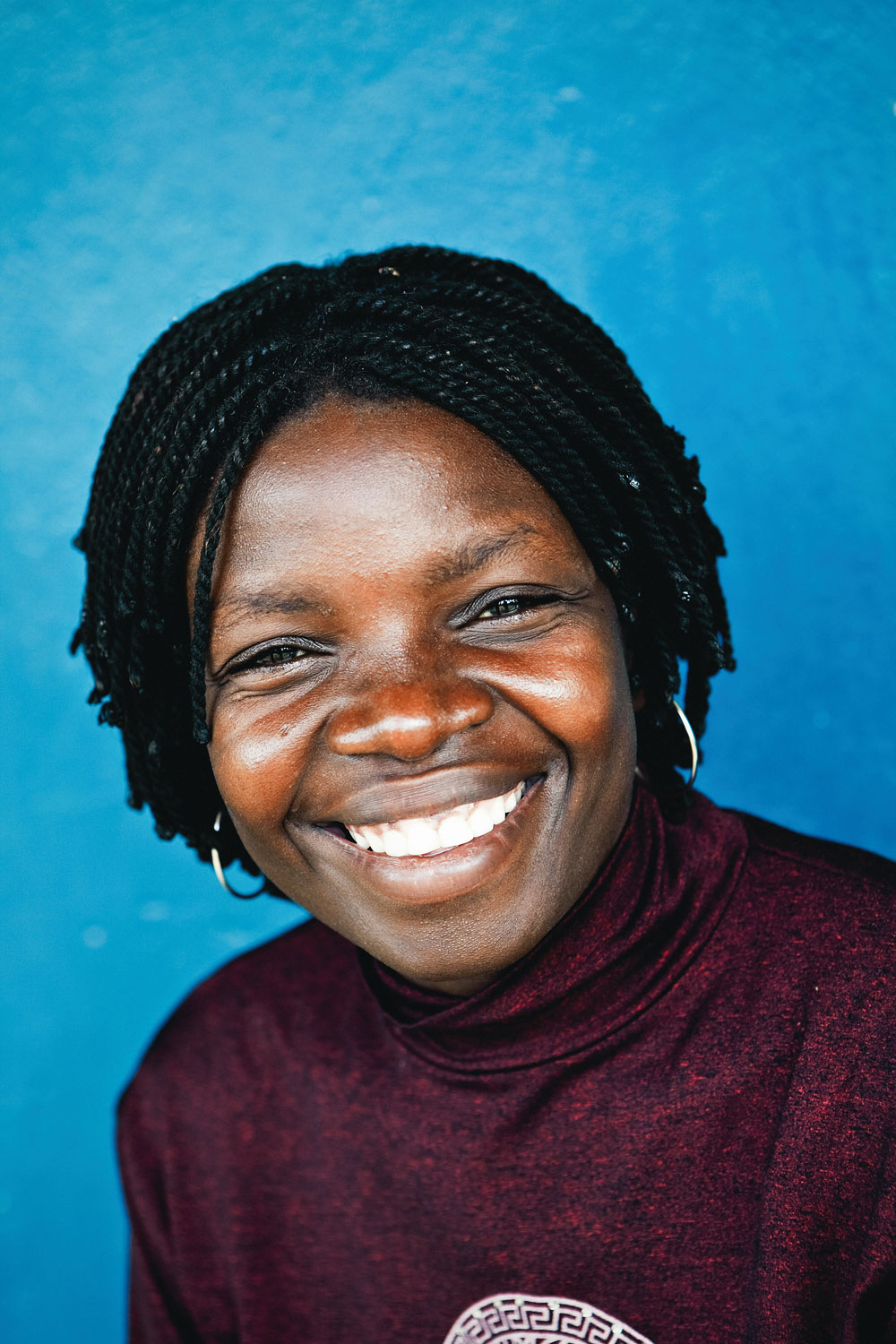 Brightly coloured headshot portrait against a blue background shot on location in rural Malawi.