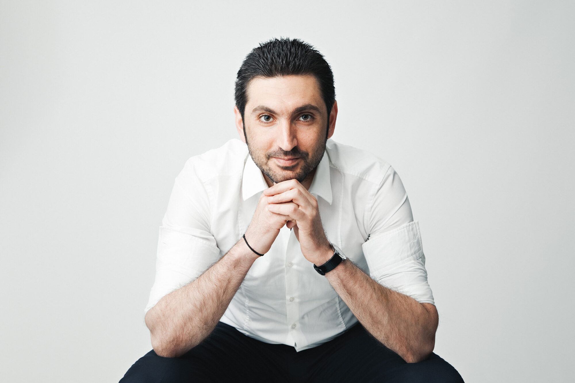 Informal corporate studio headshot of a business man against a light grey background.